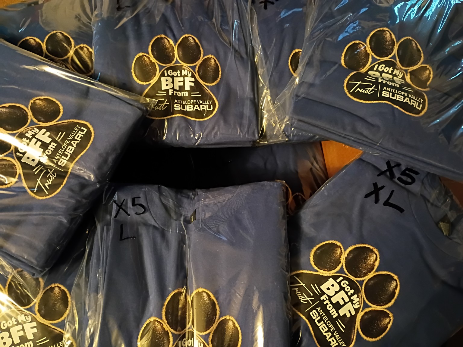 Finished blue Trust Antelope Valley Subaru BFF shirts folded and packaged together.